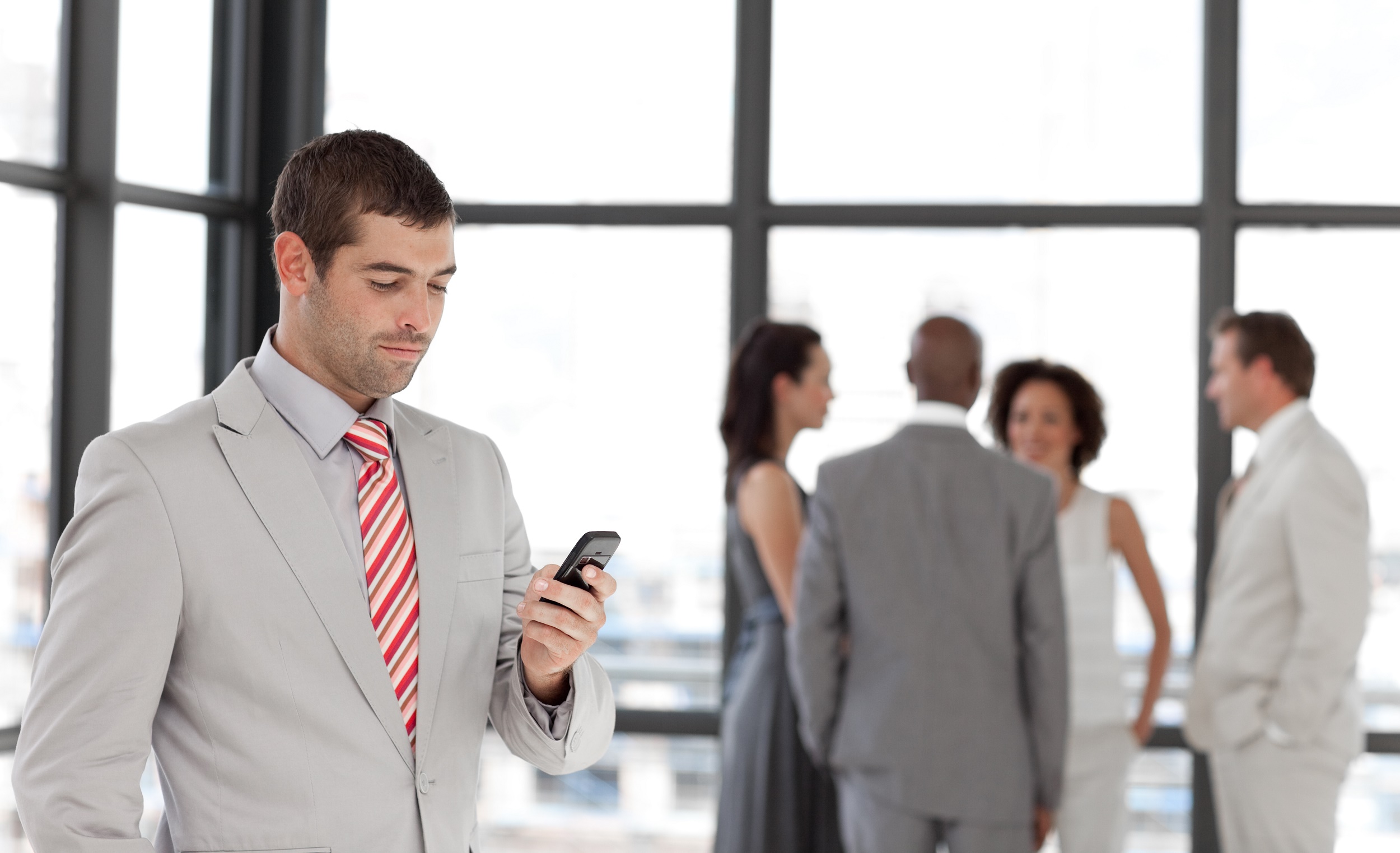 Smiling businessman holding a phone at workplace with his colleagues
