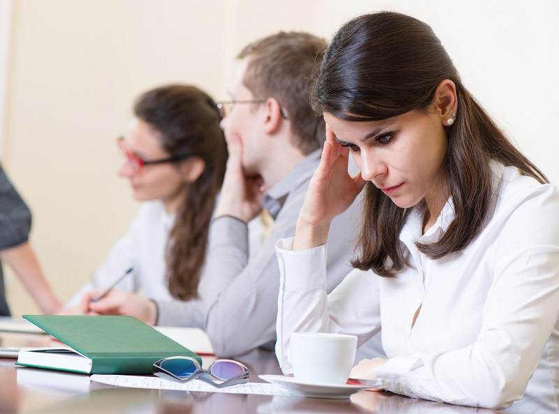 Young tired business woman with headache sitting at seminar